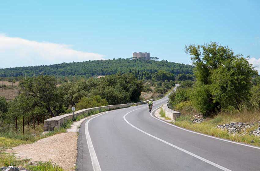Ciclista su strada con castello sullo sfondo